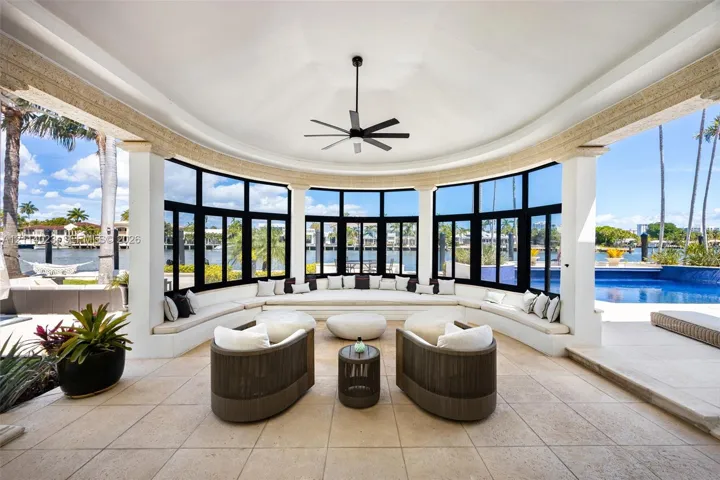Covered outdoor living space featuring a vaulted ceiling, stone tile flooring, built-in bench seating, and expansive floor-to-ceiling windows with black framing