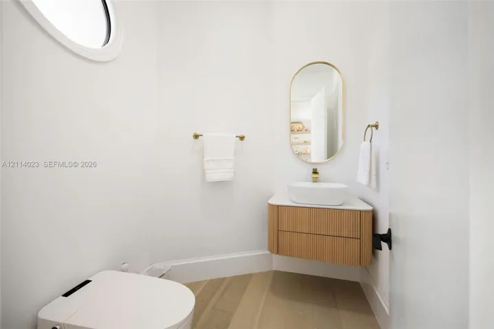 Floating wood-finish vanity with a vessel sink, oval wall mirror, wall-mounted hardware, and circular accent window