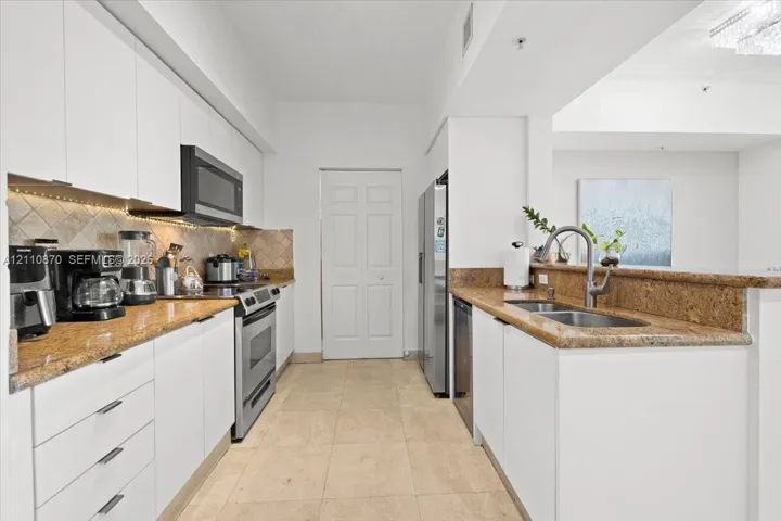Kitchen featuring white cabinetry, stone countertops, tiled backsplash, stainless steel appliances, and tile flooring