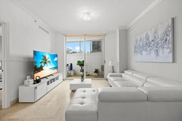 Living area featuring crown molding, neutral tile flooring, and floor-to-ceiling glass sliding doors opening to a private balcony