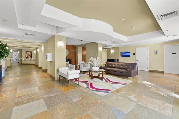 Large-scale interior featuring multi-toned stone tile flooring, an intricate coffered ceiling with recessed lighting, and wall-mounted sconces