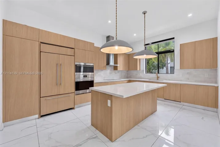 Kitchen featuring wood-finish cabinetry, quartz countertops, an oversized center island, built-in stainless steel appliances, and large-format tile flooring