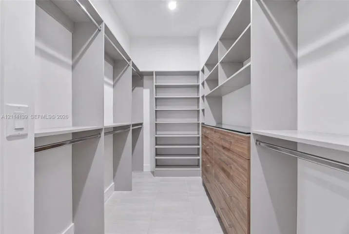 Walk-in closet featuring custom built-in shelving, wood-finish drawer cabinetry, metal hanging rods, and tiled flooring