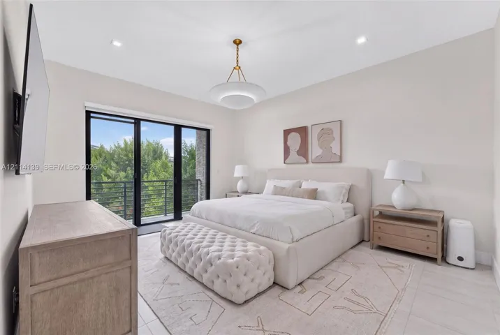 Spacious room featuring light-toned flooring, recessed lighting, a modern metal-finish pendant light, and black-framed sliding glass doors opening to a railed balcony