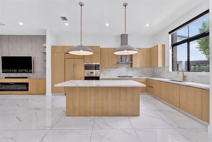 Modern kitchen featuring light-tone wood cabinetry, a center island with a stone countertop, large-format tile flooring, recessed lighting, and two pendant lights