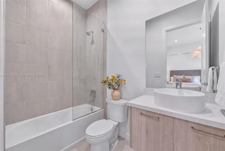 Bathroom featuring a wood-finish vanity with a stone-composite countertop, oval vessel sink, glass shower screen, and wall-to-wall mirror