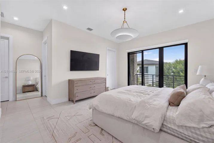 Neutral-toned tile flooring, recessed ceiling lighting, contemporary pendant fixture, and floor-to-ceiling sliding glass doors opening to a balcony with metal railings