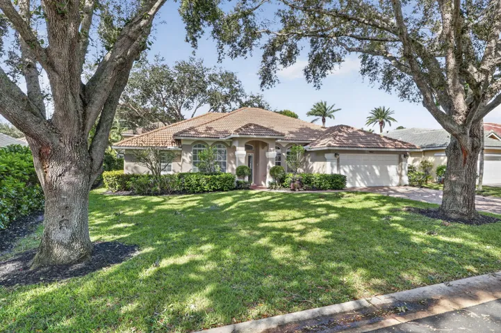 Single-story residence featuring a tile roof, arched entryway, multi-paned windows, a two-car garage, and mature landscape
