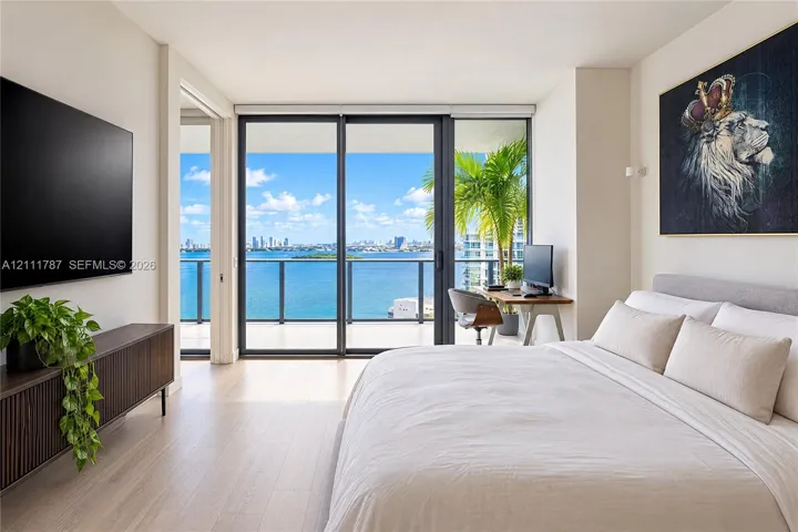 Light-toned wood-finish flooring, floor-to-ceiling sliding glass doors, and a private balcony featuring a metal railing