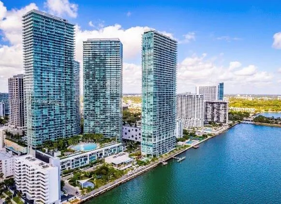 High-rise towers featuring glass-paneled balconies, floor-to-ceiling windows, and a waterfront location with an outdoor swimming pool