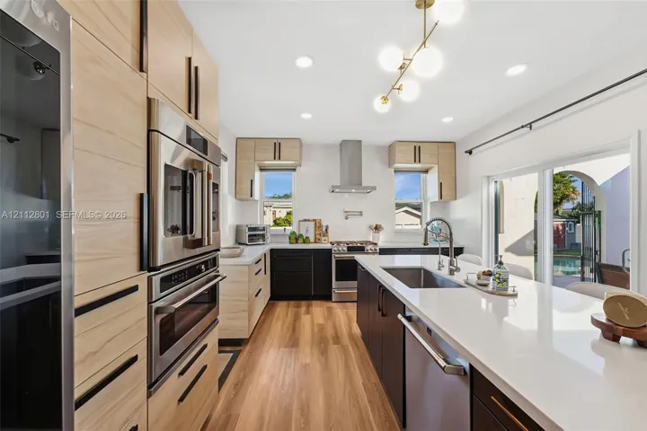Kitchen featuring two-tone cabinetry with wood-finish and matte black finishes, quartz countertops, stainless steel appliances, a center island with an undermount sink, and recessed lighting