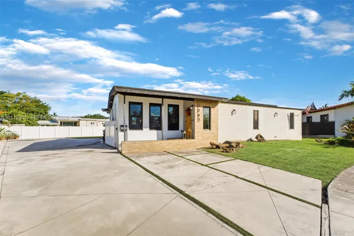 Single-story exterior featuring a stone-accented facade, covered entryway, concrete driveway with integrated turf strips, and perimeter privacy fencing