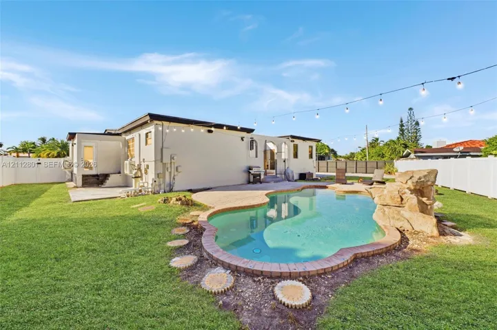 Backyard featuring an in-ground swimming pool with a stone rock feature, concrete patio, perimeter vinyl fencing, and overhead string lighting