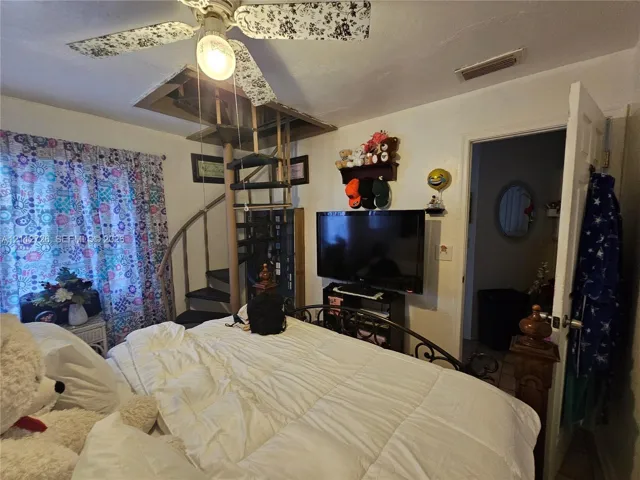 Metal spiral staircase with an integrated ceiling access hatch and a patterned ceiling fan with a central light fixture