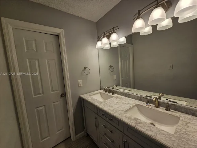 Bathroom vanity featuring dual under-mount sinks, stone-patterned countertops, gray cabinetry with metallic hardware, and two multi-bulb overhead light fixtures