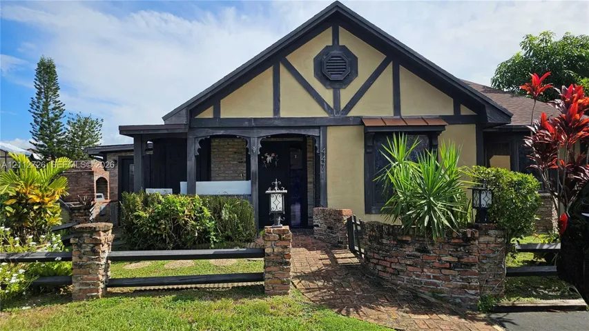 Tudor-inspired exterior featuring decorative timber framing, a brick-paved walkway, a stone-accented perimeter wall, and a built-in outdoor masonry grill