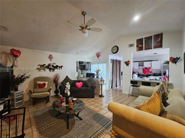 Vaulted ceilings featuring a central paddle ceiling fan, ceramic tile flooring, and a pass-through opening to the kitchen area