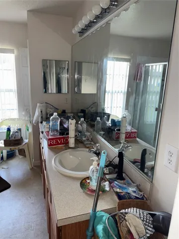 Bathroom vanity featuring a solid-surface countertop, integrated basin, chrome-finish faucet, full-width wall mirror, and overhead linear lighting