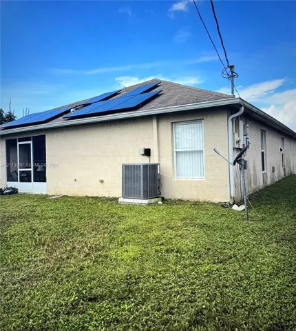 Stucco exterior featuring roof-mounted solar panels, a screened-in rear enclosure, and a central air conditioning unit