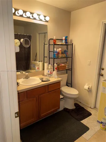 Bathroom vanity featuring wood-finish cabinetry, an integrated sink, a neutral countertop, a large wall-mounted mirror, and an overhead vanity light fixture