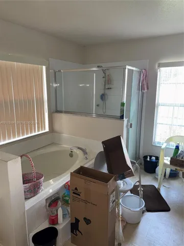 Soaking tub with chrome faucet fixtures, separate glass-enclosed shower, tile wall surrounds, and dual windows with vertical blinds