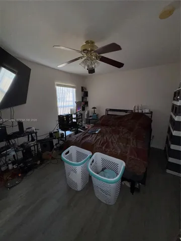 Room featuring wood-finish flooring, a multi-blade ceiling fan with integrated light fixture, and vertical window blinds