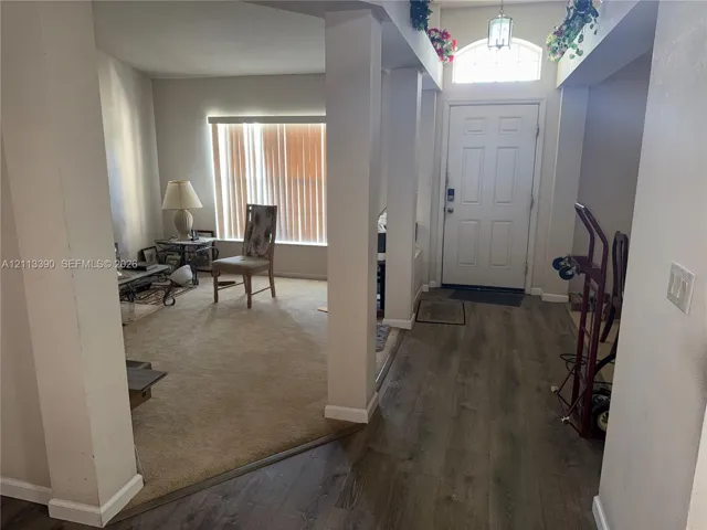 Entryway featuring wood-finish flooring, a six-panel front door with an arched transom window, and architectural support columns