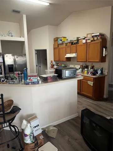 Kitchen featuring wood cabinetry, stainless steel refrigerator, neutral laminate countertops, and wood-finish flooring under vaulted ceilings