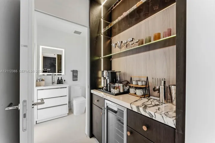 Wet bar featuring dark-toned cabinetry, integrated under-counter beverage refrigeration, and stone countertop with distinctive veining
