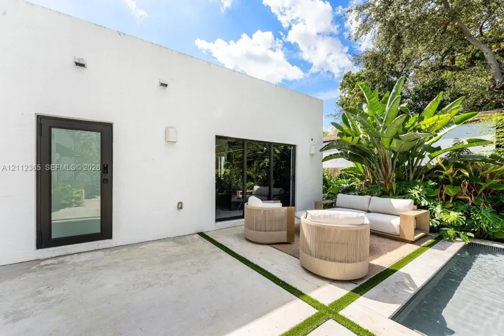Stucco exterior featuring sliding glass doors, a single-lite glass entry door, stone paver patio with integrated turf seams, and a swimming pool