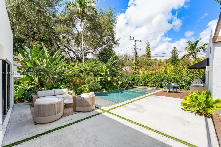 Private outdoor space featuring a pool, concrete patio with integrated turf seams, wooden deck section, and mature tropical landscaping