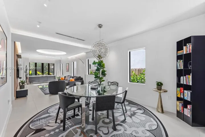 Open-concept living space featuring large-format tile flooring, a custom recessed ceiling with integrated lighting, a spherical statement chandelier, and multiple expansive windows