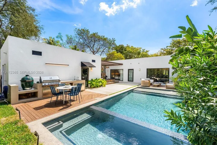 Outdoor patio featuring a custom concrete kitchen with built-in stainless steel appliances, wood-finish decking, and a swimming pool with integrated tanning ledge