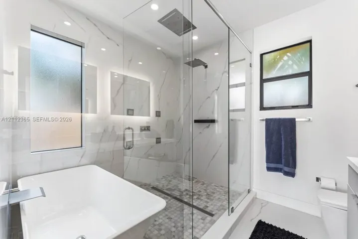 Bathroom featuring a soaking tub, glass-enclosed walk-in shower with rainfall showerhead, and stone-finish wall tile