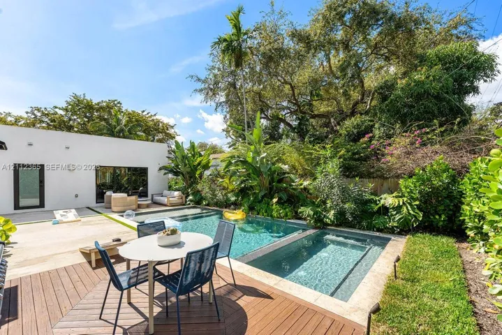 Rear outdoor space featuring an in-ground pool with stone coping, tiered wood-finish decking, and professional landscaping
