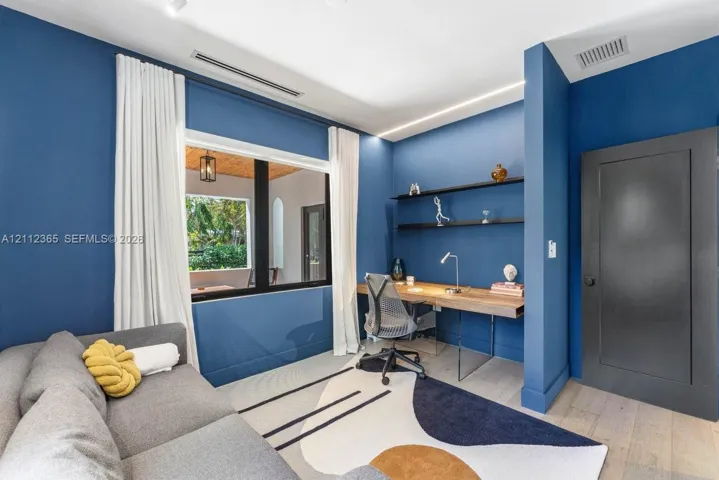 Room featuring wood-finish flooring, recessed ceiling lighting, built-in wall shelving, a wall-mounted desk, and black paneled door