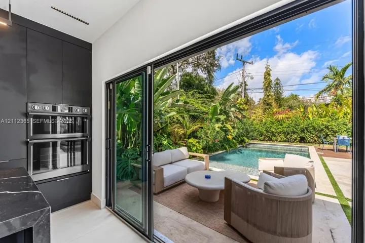 Full-height glass sliding doors, built-in dual wall ovens, dark cabinetry, stone-finish countertops, and an exterior swimming pool