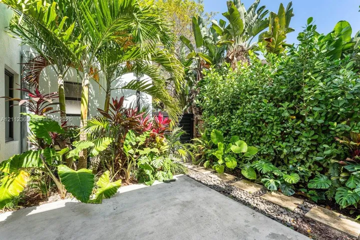 Private outdoor area featuring a concrete patio, stone paver border, river rock accents, and established tropical landscaping