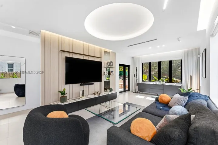 Living area featuring a custom vertical-slat accent wall with integrated shelving, recessed circular ceiling lighting, large-format tile flooring, and a low-profile media console with stone-finish countertop