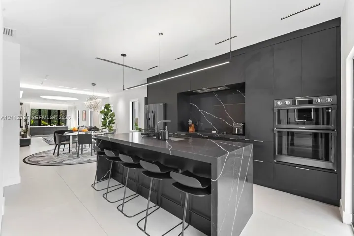 Kitchen featuring matte black floor-to-ceiling cabinetry, dark stone-finish waterfall island with waterfall edge, integrated stainless steel double wall oven, and linear pendant lighting