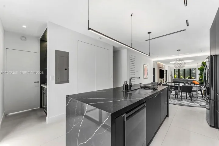 Kitchen island featuring dark veined stone surfacing, integrated cabinetry, undermount sink with a gooseneck faucet, and linear pendant lighting