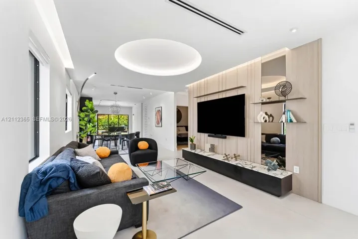 Living area featuring a custom wood-panel accent wall, integrated media console, recessed circular ceiling lighting, mirrored wall accents, and large-format flooring