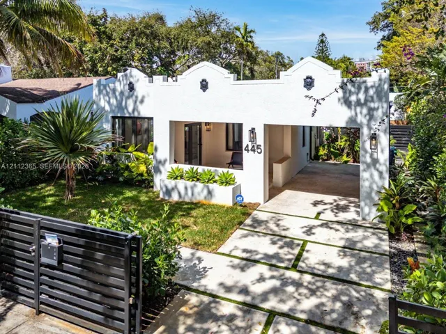 Stucco exterior featuring decorative corbels and parapet roofline, integrated covered carport, paved driveway with grass inlays, and built-in masonry planter
