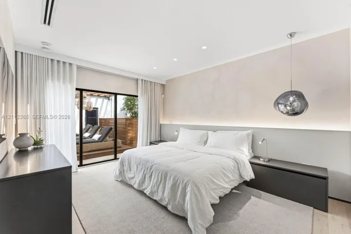 Floor-to-ceiling sliding glass doors, built-in recessed lighting, integrated wall-mounted headboard with accent lighting, and sculptural glass pendant fixture