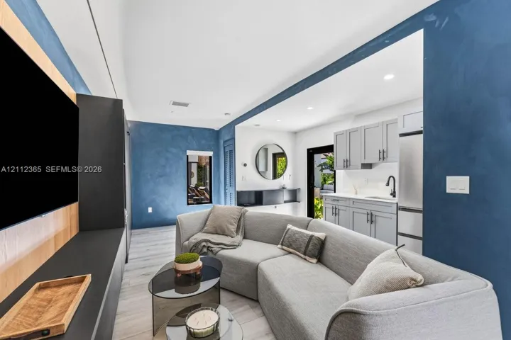Textured blue feature walls paired with wood-finish flooring, custom built-in cabinetry, recessed lighting, and a kitchenette featuring Shaker-style cabinetry with a matte black faucet
