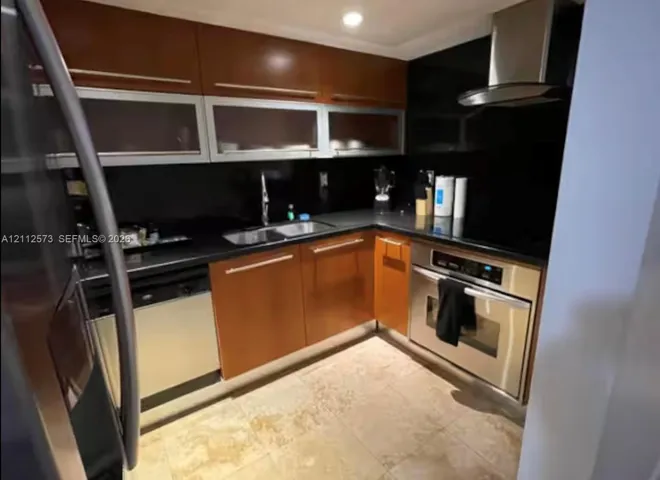 Kitchen featuring wood-finish cabinetry, solid surface countertops, glass-panel upper cabinets, stainless steel appliances, and a range hood