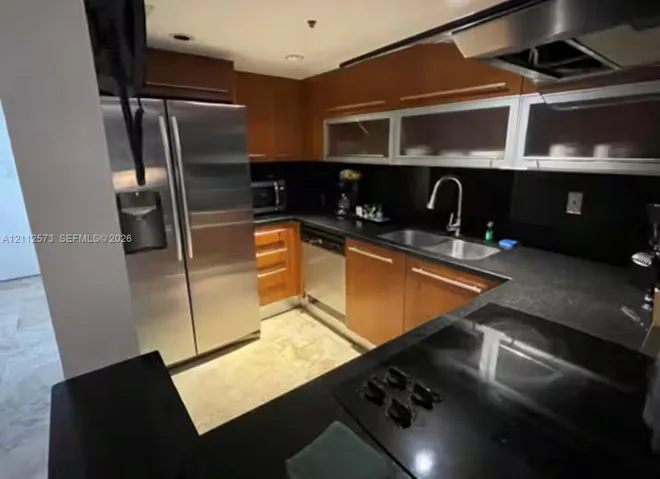 Kitchen featuring custom wood cabinetry, stainless steel appliances, dark countertops, a gooseneck faucet, and upper cabinets with glass-panel inserts