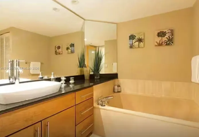 Built-in cabinetry with natural wood finish, dark stone countertop, rectangular vessel sink with single-handle faucet, and integrated soaking tub with chrome hardware