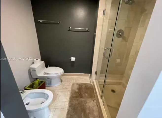 Bathroom featuring a walk-in shower with a glass enclosure, wall-mounted chrome hardware, stone-tile flooring, and a bidet