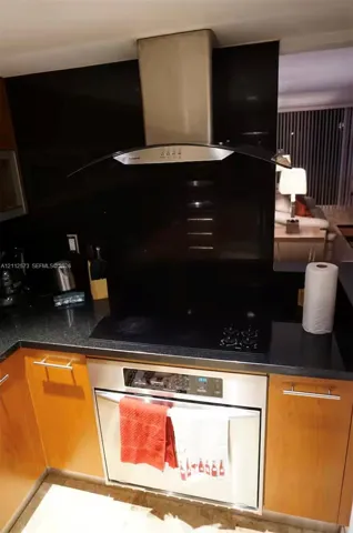 Stainless steel oven with an integrated stovetop, stainless steel range hood, dark solid-surface countertops, and wood-finish cabinetry with bar hardware